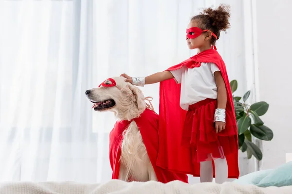 Side view of cute little african american kid and dog standing on the bed — Stock Photo