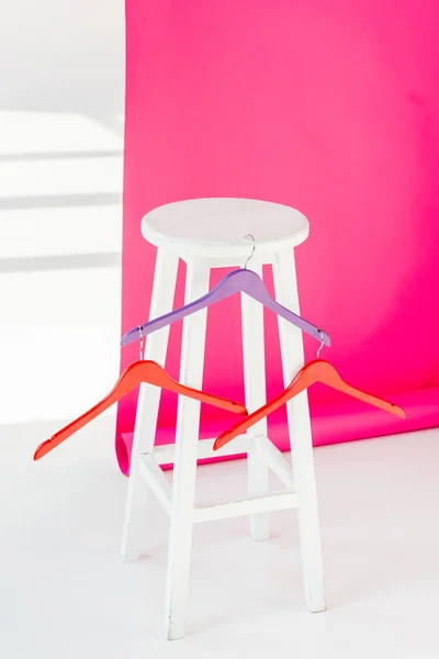 Multicolored painted hangers with white wooden chair and pink wallaper — Stock Photo