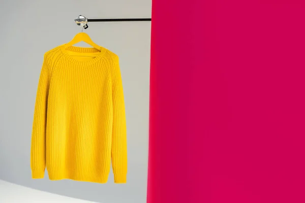 Knitted yellow sweater on hanger on pink and grey background — Stock Photo