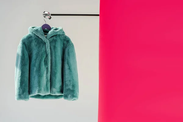 Primo piano di soffice pelliccia verde finto cappotto su appendino con carta da parati rosa — Foto stock