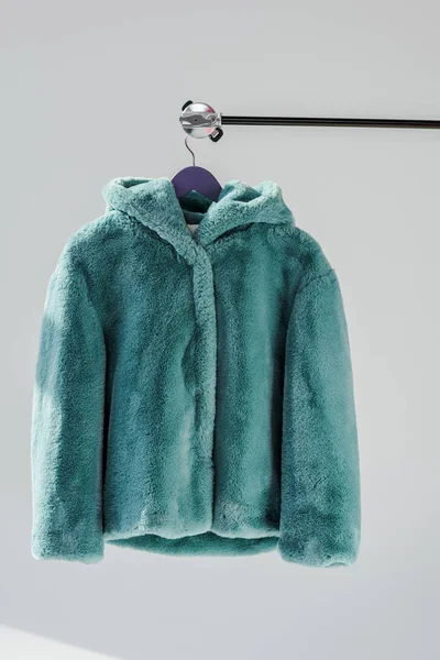 Close up of fluffy green faux fur coat hanging on rack at grey background — Stock Photo