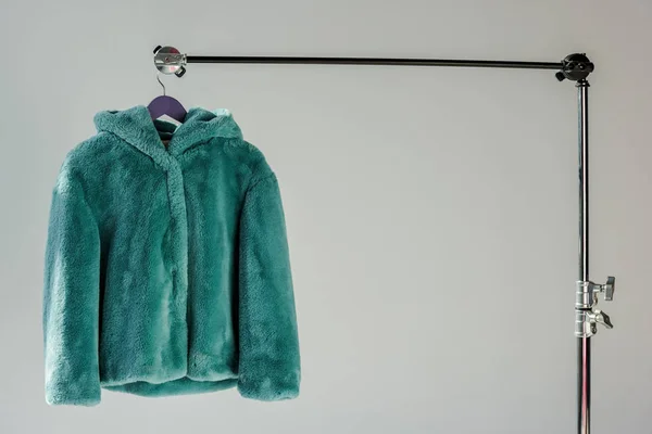 Fluffy green faux fur coat hanging on rack at grey background with sunbeams — Stock Photo
