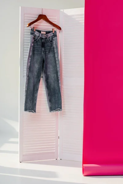 Jeans hanging on white room divider with pink rolled out wallpaper — Stock Photo