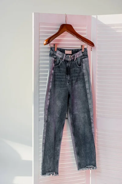Primo piano di jeans appesi a divisorio di camera bianco con raggi di sole — Foto stock