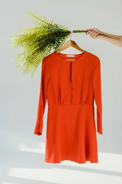 Mão feminina segurando cabide com vestido elegante vermelho e plantas verdes — Fotografia de Stock