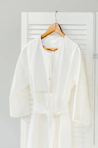 Nahaufnahme eines eleganten weißen Kleides, das an einem hölzernen Raumteiler hängt, isoliert auf grau — Stockfoto