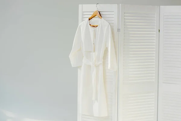 Elegantes weißes Kleid hängt an hölzernem Raumteiler — Stockfoto