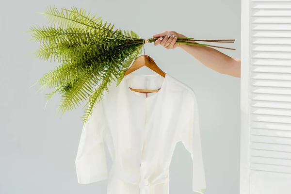 Крупним планом жіноча рука тримає вішалку з білим платтям і зеленими рослинами — стокове фото