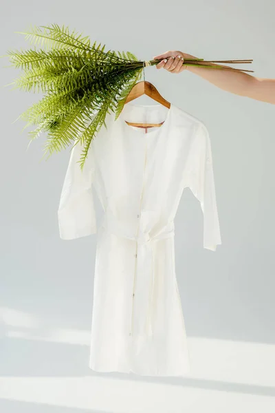 Female hand holding hanger with white dress and green plants — Stock Photo