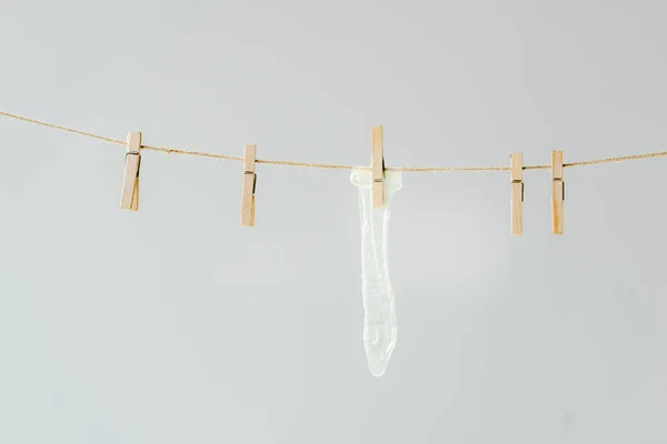 Raw of wooden clothespins with white condom hanging on clothesline isolated on grey — Stock Photo