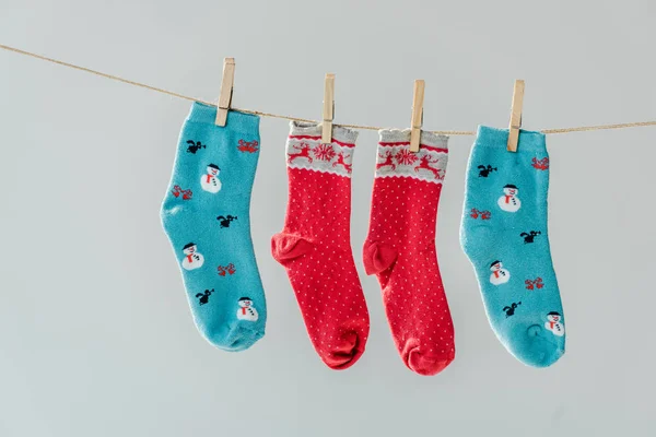 Gros plan de chaussettes de fête d'hiver multicolores accrochées à une corde à linge avec des pinces isolées sur du gris — Photo de stock