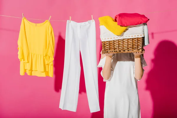 Женщина прячет лицо за плетеной корзиной с висящей одеждой на заднем плане — стоковое фото
