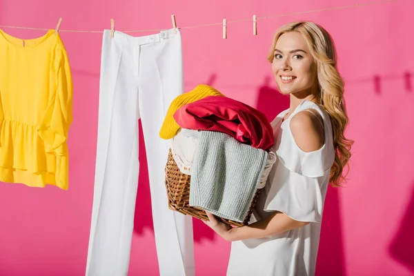 Smiling woman holding wicker basket with hanging clothes at background — Stock Photo