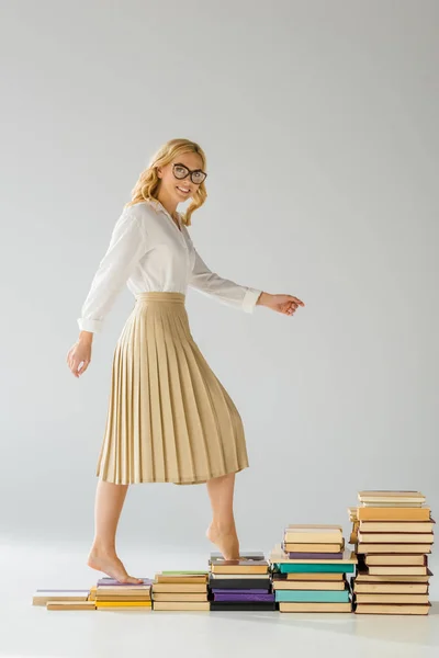 Mujer sonriente en gafas caminando sobre escalones hechos de libros - foto de stock