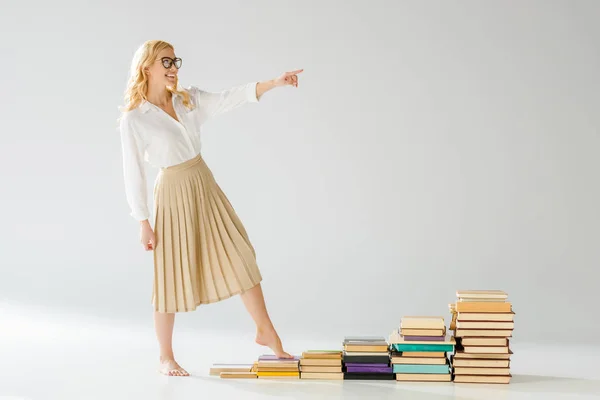 Счастливая женщина в очках, идущая по ступенькам из книг — стоковое фото
