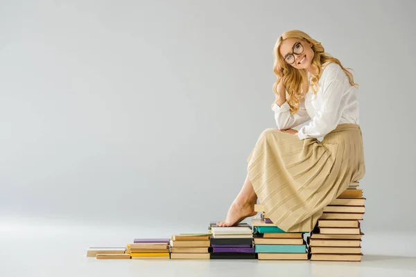 Glückliche barfüßige Frau mit Brille, die auf Stufen aus Büchern sitzt — Stockfoto