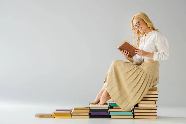 Attraktive lächelnde barfüßige Frau mit Brille sitzt auf Stufen aus Büchern — Stockfoto