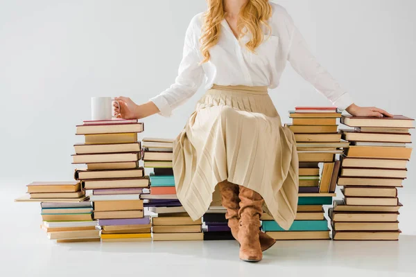Крупним планом доросла жінка сидить на купі книг з чашкою — стокове фото
