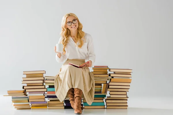 Sorrindo bela mulher bebendo café e sentado em pilha de livros — Fotografia de Stock