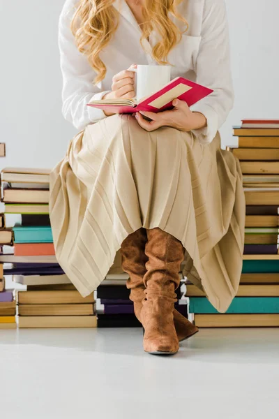 Primo piano di donna che beve caffè, legge e si siede su mucchio di libri — Foto stock