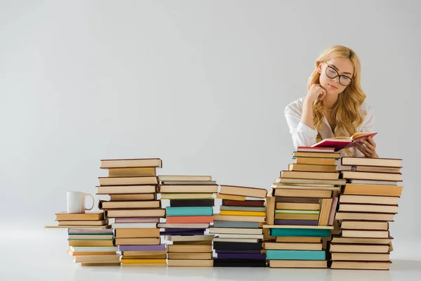 Bella donna in occhiali lettura vicino mucchio di libri — Foto stock