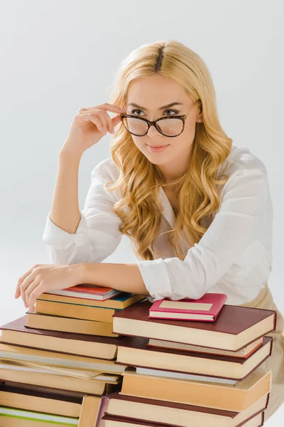 Красива жінка тримає окуляри біля купи книг ізольовані на сірому — стокове фото
