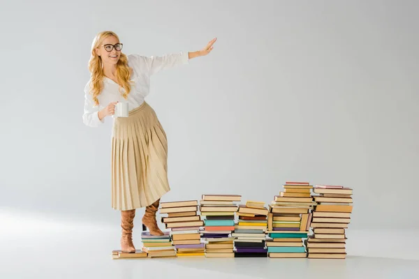 Adulto elegante mujer de pie en los libros con blanco taza - foto de stock
