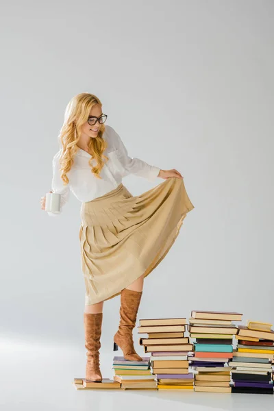 Erwachsene elegante Frau steht auf Büchern mit weißer Tasse — Stockfoto