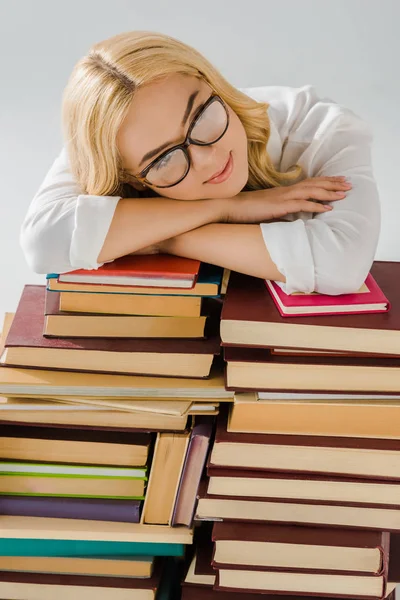 Мечтающая женщина в очках, лежащая на куче книг, изолированных на сером — стоковое фото