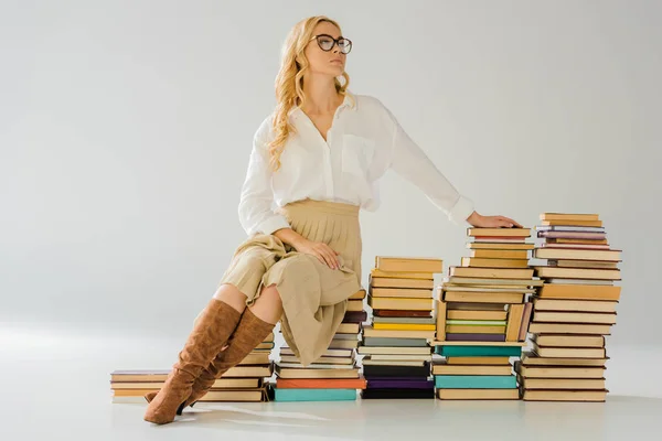 Schöne blonde Frau mit Brille sitzt auf einem Stapel Retro-Bücher — Stockfoto