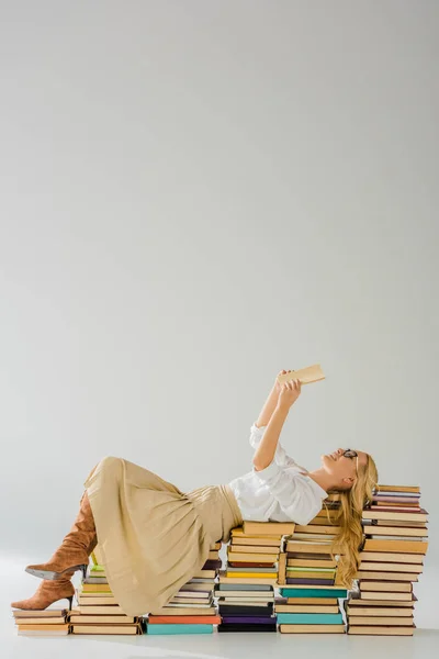 Beautiful blonde woman in glasses reading and laying on pile of retro books — Stock Photo