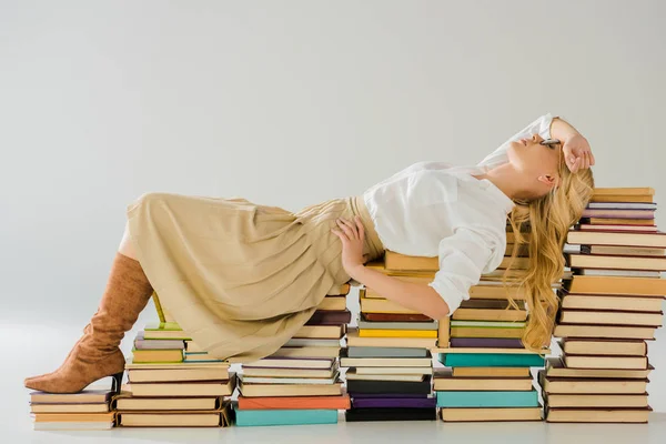 Beautiful blonde woman in glasses posing on pile of retro books — Stock Photo