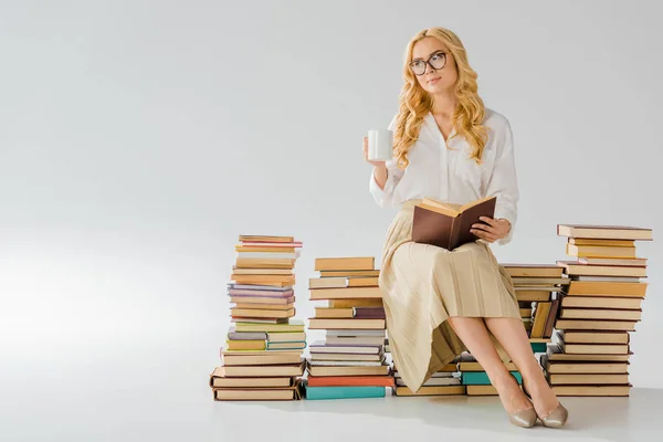 Bella donna adulta seduta su mucchio di libri retrò con tazza bianca — Foto stock