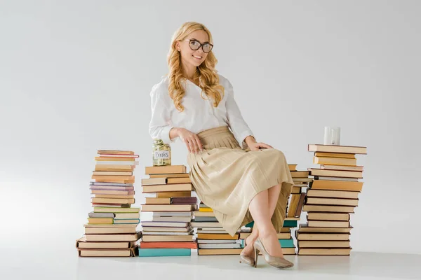 Hermosa mujer en gafas sentado en libros con ahorros en frasco y taza - foto de stock
