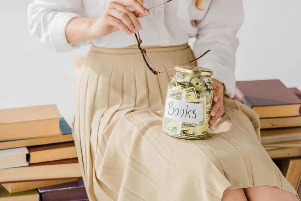 Close up of woman sitting on books with money savings in jar — Stock Photo