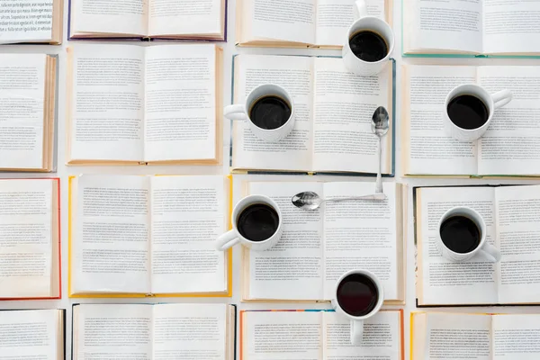 Верхний вид на часы из белых чашек с кофе и ложки на открытых книгах — стоковое фото