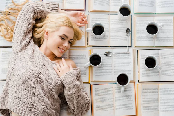 Lächelnde Frau, die neben der Uhr aus weißen Tassen mit Kaffee und Löffeln auf offenen Büchern liegt — Stockfoto