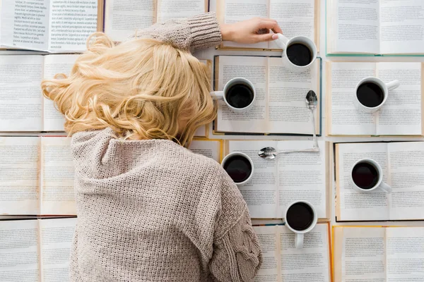 Müde Frau liegt neben Uhr aus weißen Tassen mit Kaffee und Löffeln auf aufgeschlagenen Büchern — Stockfoto