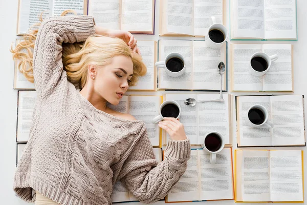 Woman laying near clock made of white cups with coffee and spoons on open books — Stock Photo