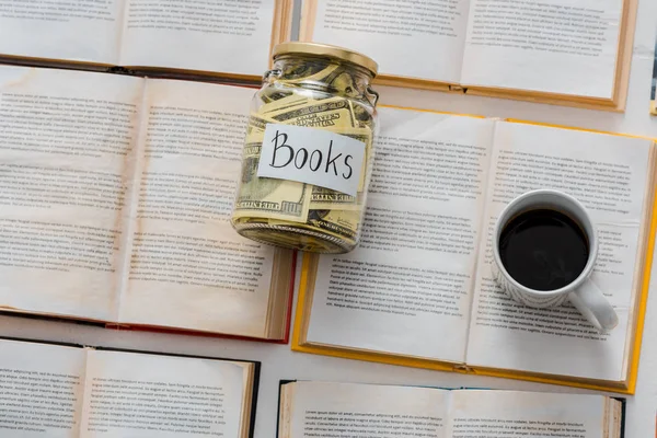 Close up of money savings in jar with cup of coffee on open books — Stock Photo
