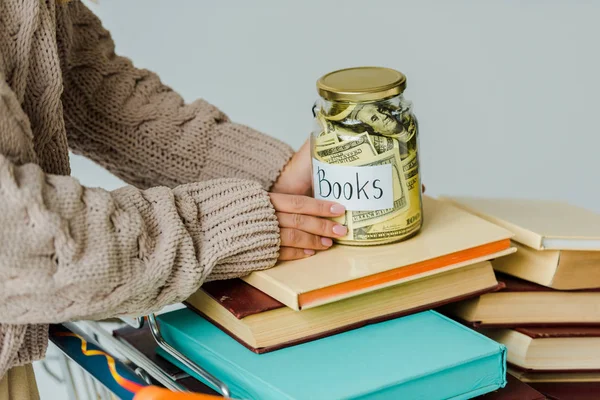 Gros plan des mains féminines tenant le bocal avec de l'argent sur les livres — Photo de stock