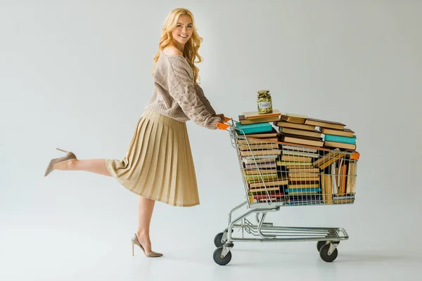 Красивая женщина с деньгами в банке и ретро-книги в корзине изолированы на серый — стоковое фото