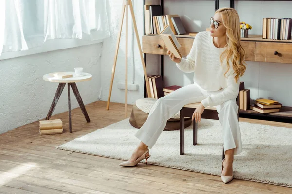 Belle femme adulte dans des lunettes assis sur la chaise et le livre de lecture — Photo de stock