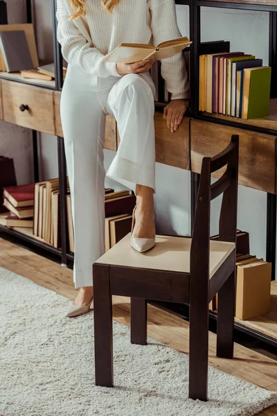 Close up of adult woman sitting on rack in living room and reading book — Stock Photo