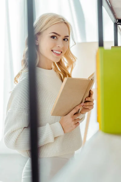 Крупним планом красива усміхнена жінка читає книгу у вітальні — стокове фото