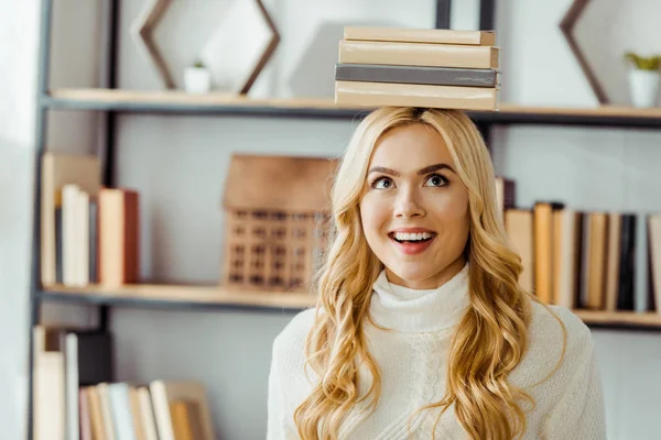 Primer plano de la mujer sonriente divertida con libros en la cabeza - foto de stock
