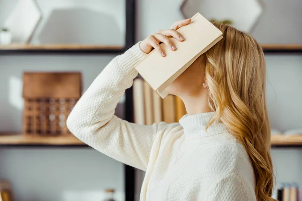 Primer plano de la mujer rubia poniendo libro en la cara - foto de stock