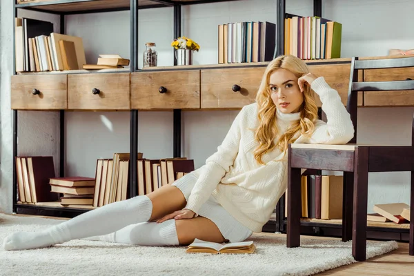 Hermosa mujer sentada en la alfombra con libro en la sala de estar - foto de stock