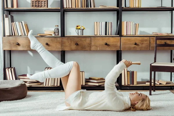 Lächelnde Frau legt sich auf Teppich und liest Buch — Stockfoto