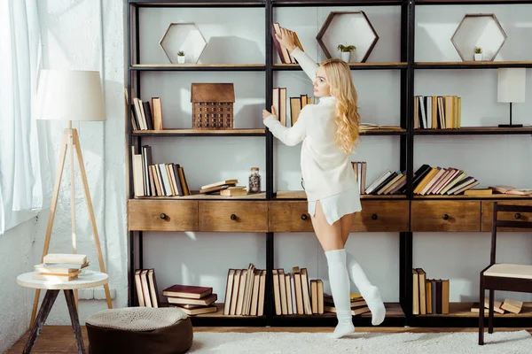 Beautiful adult woman taking book from wooden rack — Stock Photo